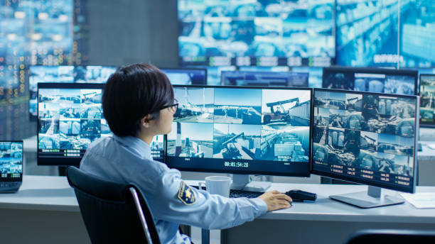 istock In the Security Control Room Officer Monitors Multiple Screens for Suspicious Activities, He Drinks from a Mug. He's Surrounded by Monitors and Guards Port of National Importance. 890156760