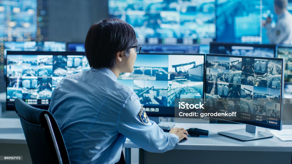 In the Security Control Room Officer Monitors Multiple Screens for Suspicious Activities. He's Surrounded by Monitors and Guards Facility of National Importance. Security Stock Photo