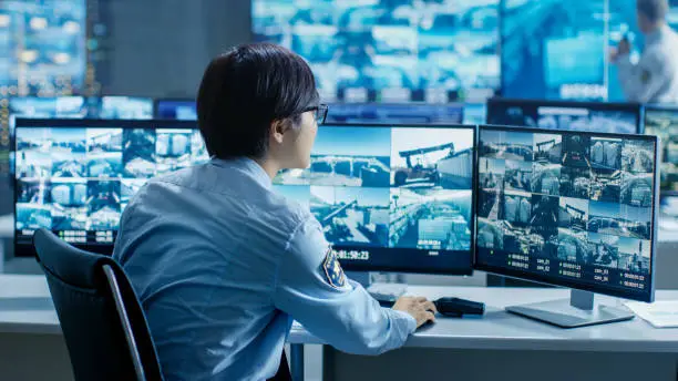 In the Security Control Room Officer Monitors Multiple Screens for Suspicious Activities. He's Surrounded by Monitors and Guards Facility of National Importance.