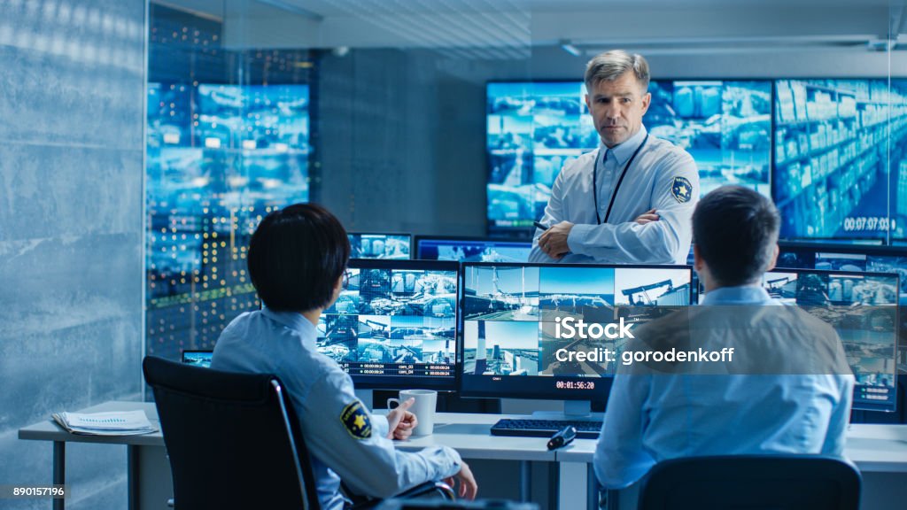 In the Security Control Room Chief Surveillance Officer Holds a Briefing for Two of His Subordinates. Multiple Screens Show that They Guard Object of International Importance. Security Stock Photo