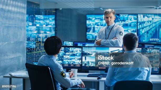 In The Security Control Room Chief Surveillance Officer Holds A Briefing For Two Of His Subordinates Multiple Screens Show That They Guard Object Of International Importance Stock Photo - Download Image Now