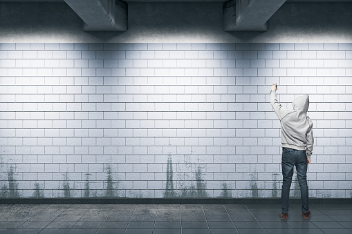 Back view of young hipster man with hood painting graffiti in subway station. Vandalism concept. Mock up, 3D Rendering