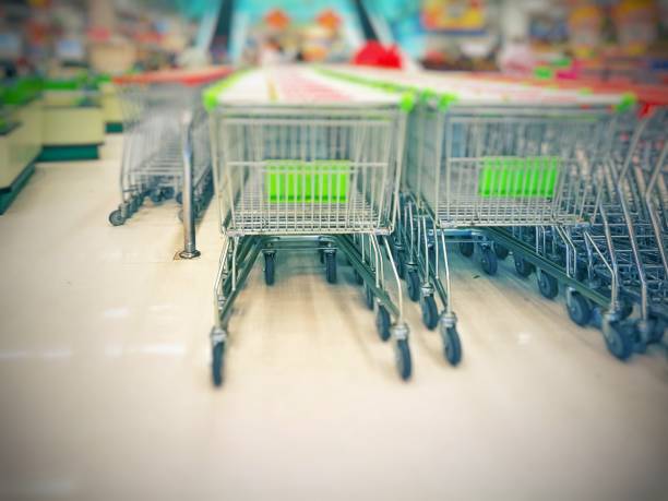 istock Blurred empty shopping carts (green and white handles) in a large supermarket 890221426