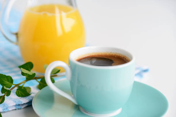 Strong black coffee in a light blue cup on a white table with orange juice.