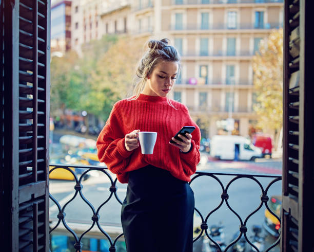 Young girl is texting using her mobile phone at the balcony Young girl is texting using her mobile phone at the balcony coffee addict stock pictures, royalty-free photos & images