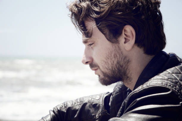istock Pensive man sitting in front of the ocean serious side shot 890264320