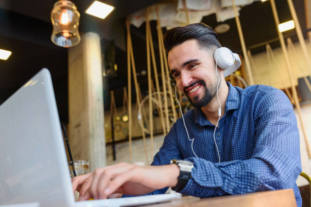 istock Cheerful Young Man Using Tablet with Earphones In Coffee Shop 890281966