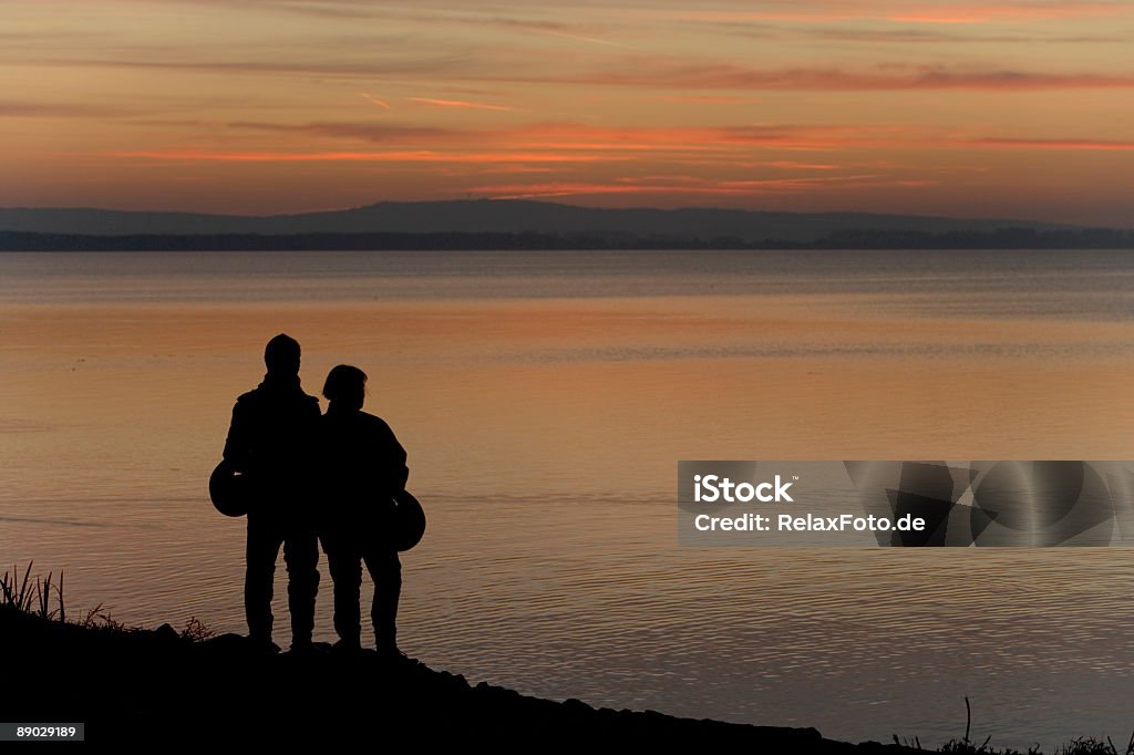 Пара, наблюдая закат на берегу озера motorbikers (XXL) Облачный пейзаж - Стоковые фото Озеро роялти-фри