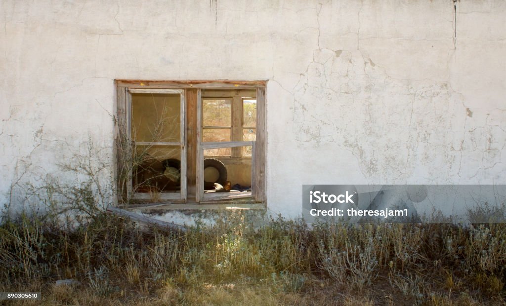 abandoned old house old adobe house abandoned looking at the wall closeup and peering through two windows with old tires while the sun gleams through one wooden window Abandoned Stock Photo