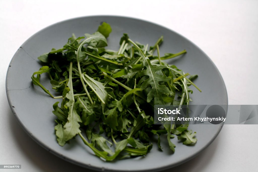 Heap of arugula on plate Heap of arugula salad isolated on gray concrete plate Arugula Stock Photo