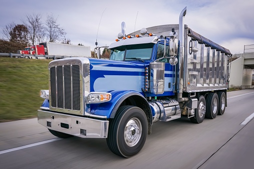 Blue chrome dump truck driving on highway with 18 wheeler in the background