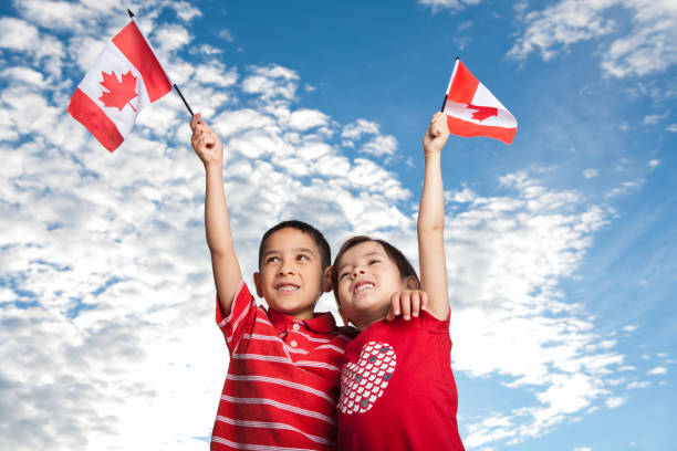 Young sibling celebrating Canada Day Kids waving Canadian Flag against sky canada flag blue sky clouds stock pictures, royalty-free photos & images