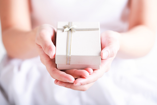Close up of female hands holding a small gift wrapped with ribbon. Christmas concept