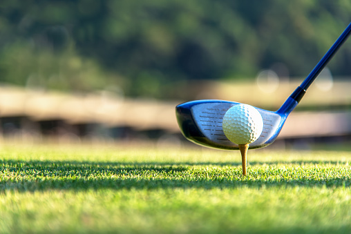 Cerca de la pelota de golf y un conductor, jugador haciendo golf swing tee off en el verde tiempo de la puesta del sol de la tarde, presumiblemente del ejercicio.  Saludable y el concepto de estilo de vida. photo