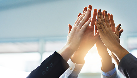 Low angle shot of a group of businesspeople high fiving while standing in their office