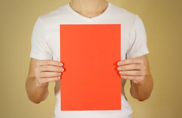istock Man holding red A4 paper vertically. Leaflet presentation. Pamphlet hold hands. Man show clear offset paper. Sheet template. Booklet design sheet display read first person 890554328