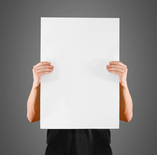 istock Man showing blank white big A2 paper, covers the face. Leaflet presentation. Pamphlet hold hands. Man show clear offset paper. Sheet template. Booklet design sheet display read first person. 890554672