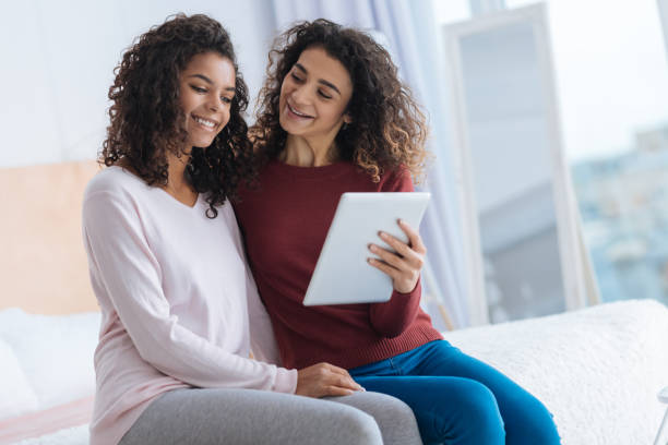 istock Curious young lady holding touchpad and smiling to her sister 890584126