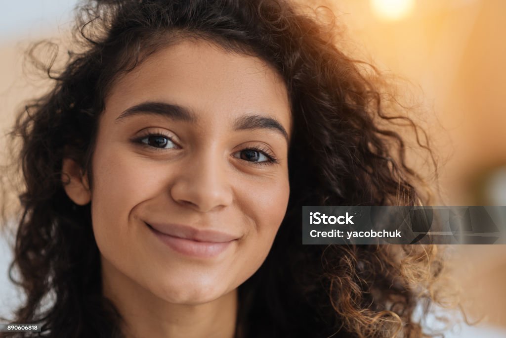 Portrait of beautiful young brunette beaming into camera Heavenly beauty. Charming curly haired young lady looking into the camera with eyes full of happiness and smiling cheerfully indoors. Women Stock Photo