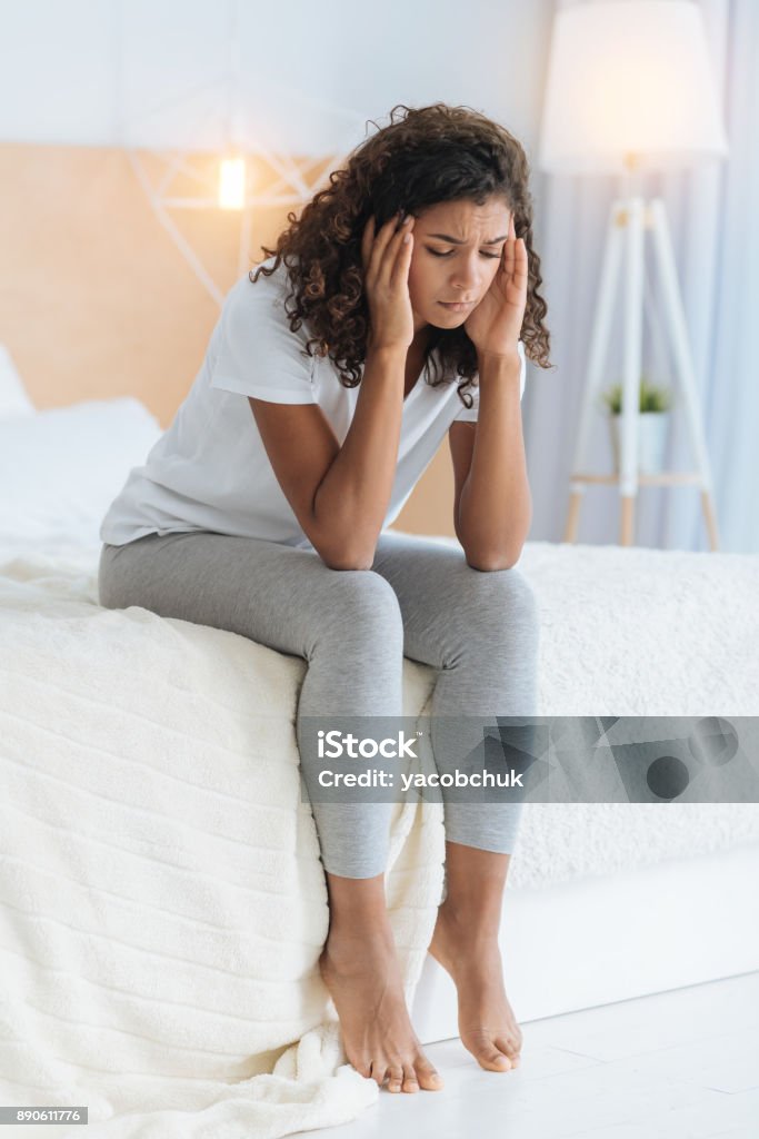 Poor girl messaging her temples while having headache This hurts so much. Full length shot of a tired young lady touching her temples while sitting on a bed and feeling some physical discomfort. Women Stock Photo