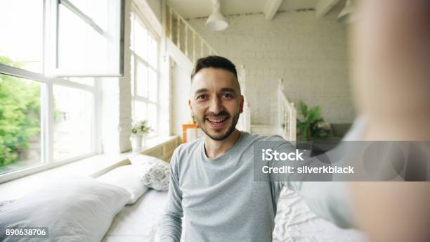 Young Bearded Man Using Tablet Computer Having Video Chat Sitting In Bed At Home Stock Photo - Download Image Now