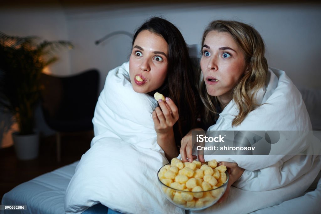 Captivating movie Curious girls eating corn rolls from bowl while watching captivating movie at night Movie Stock Photo