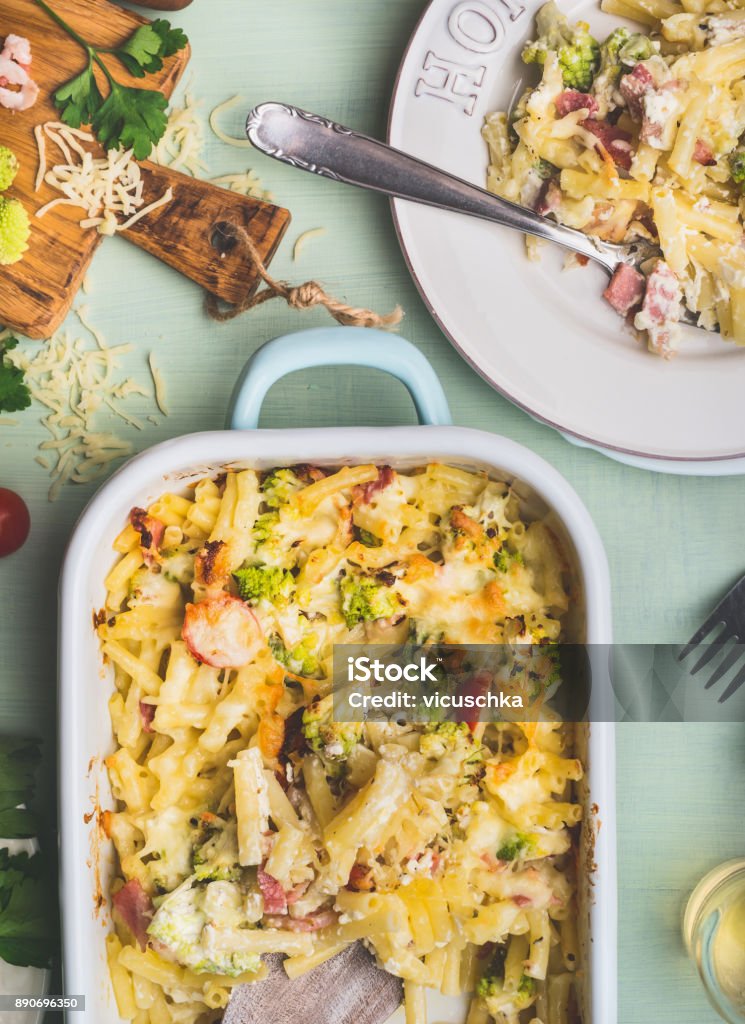 Pasta casserole with romanesco cabbage and ham in creamy sauce,  served in plate with fork on kitchen table with ingredients Pasta casserole with romanesco cabbage and ham in creamy sauce,  served in plate with fork on kitchen table with ingredients, top view, close up.  Italian cuisine Casserole Stock Photo