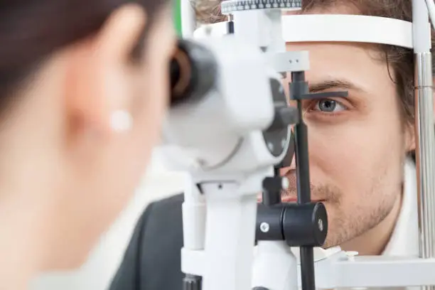 Slit Lamp eye control with the Ophthalmologist / handsome man during a contact lenses examining / the oculist in eyes clinic doing cornea and retina exam diagnostic / high technology concept eyes care