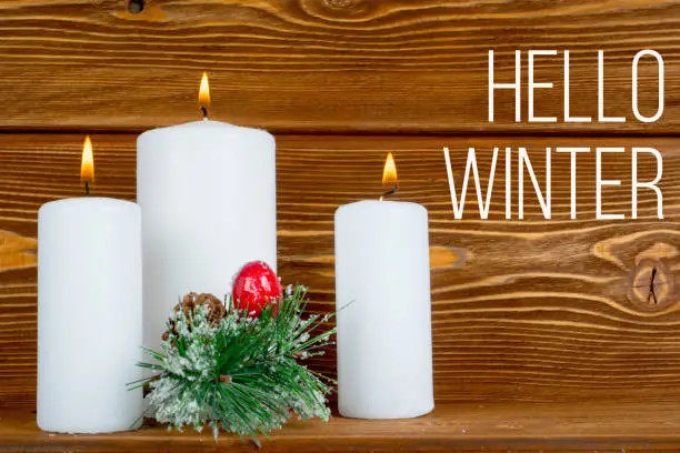 hello winter, text over wooden planks with 3 burning candles and pine tree branch