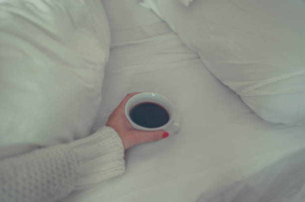 istock Woman's hand holding a cup of coffee on white bed 890747548