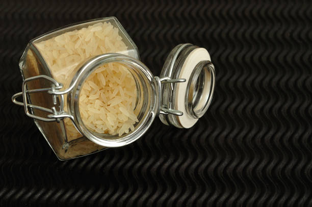 istock Uncooked rice in a jar displayed on a black background. 890771562