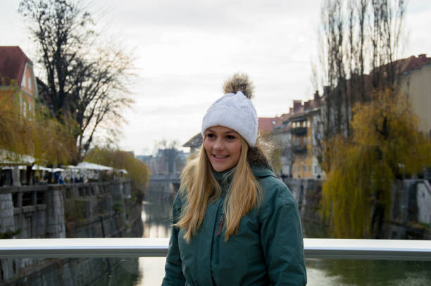 Winter city girl A smiling woman is standing on a bridge across the Ljubljanica river. It's cold, so she is wearing warm winter clothing and a white knit hat. cheesy grin photos stock pictures, royalty-free photos & images