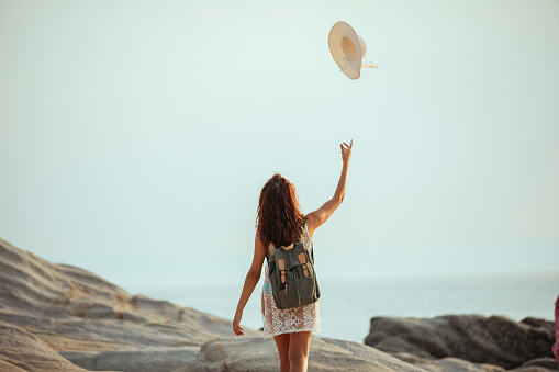 Young woman walking on the beach , trowing her hat in the air