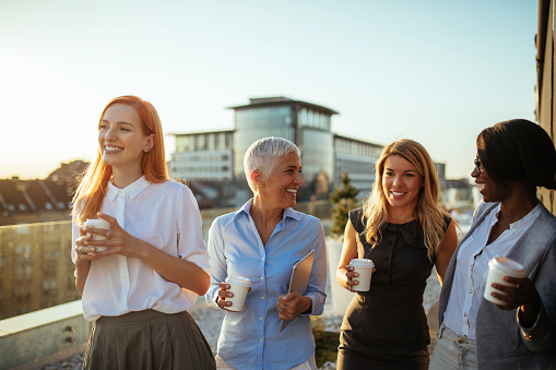 Group of businesswomen on the rooftop holding paper cups laughing