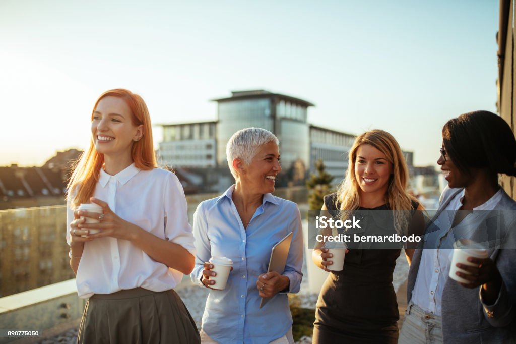 Happiness inspires productivity Group of businesswomen on the rooftop holding paper cups laughing Group Of People Stock Photo