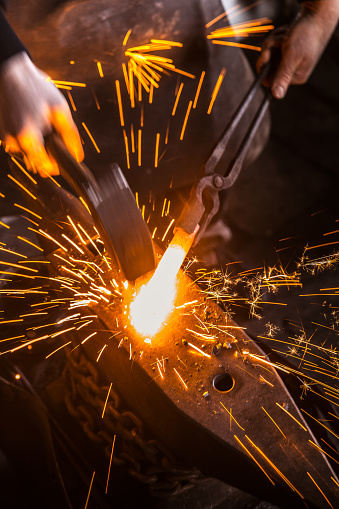 Blacksmith hitting hot metal rod with hammer on anvil