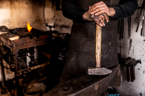 Shot of blacksmith in his workshop in Malaysia. He is bending iron rods on anvil.
