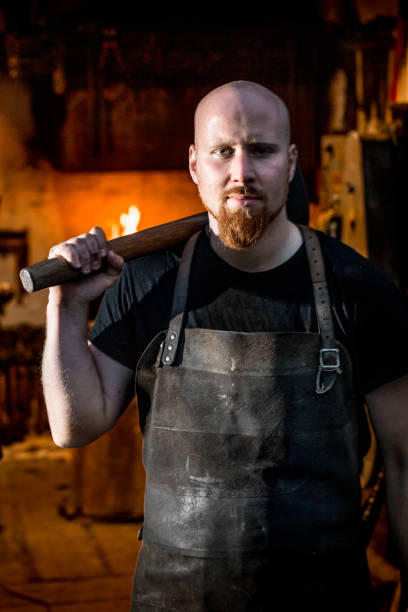 istock Blacksmith Holding a Hammer Over his Shoulders, Forge in the Background 890775344