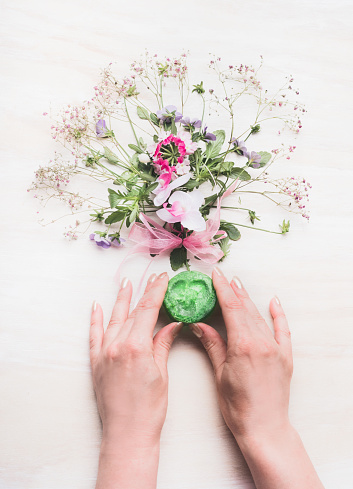 Female hands holding natural handmade green soap with fragrant herbs and flowers ,  Organic Soap making, top view. Cosmetic, skincare and beauty concept
