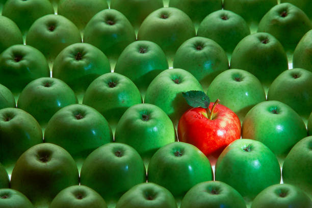 one red apple among many green apples stock photo