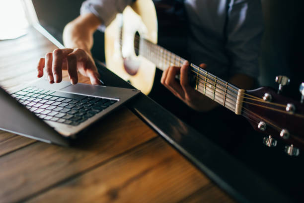 online music courses learn play guitar online music courses. young man learns how to play guitar through the internet. modern technology education benefits concept music theory stock pictures, royalty-free photos & images