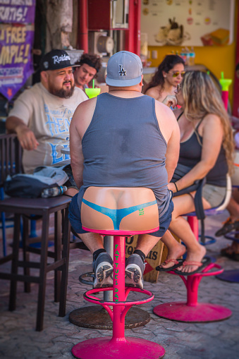 Playa del Carmen, Mexico - march 28, 2017:  In this resto-bar on 5th avenue, the stools are funny and make passers-by laugh. This tough man who is seen from behind is sitting in a bench that makes him believe he is wearing a delicate panties of a woman ....