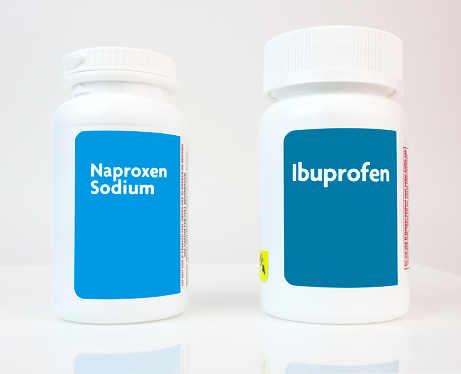 Two generic white plastic bottles of popular over-the-counter pain relievers- ibuprofen and naproxen. Horizontal.