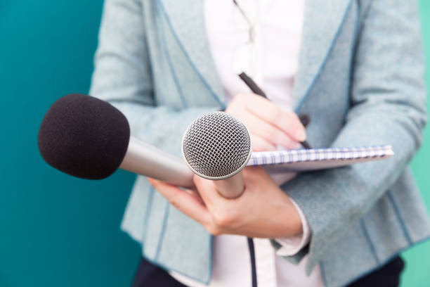 istock Female journalist at news conference, writing notes, holding microphone 890831398
