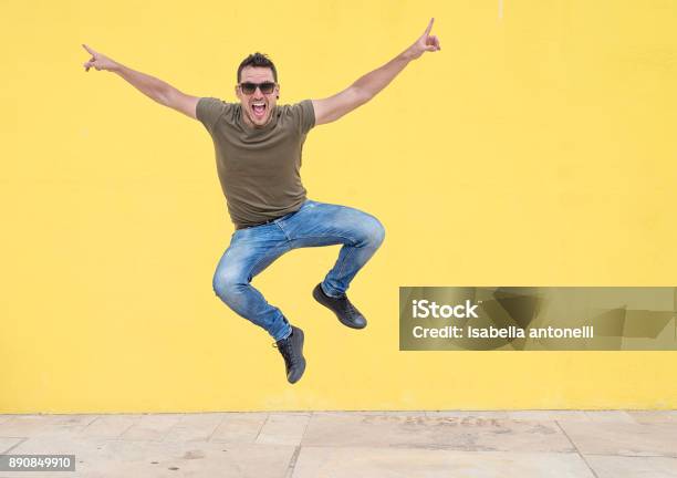 Young Man With Sunglasses Jumping In Front Of A Yellow Wall Stock Photo - Download Image Now