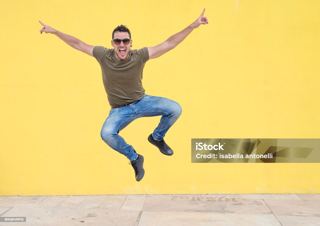 Jovem com óculos de sol saltar na frente de uma parede de amarela. - Foto de stock de Dia royalty-free