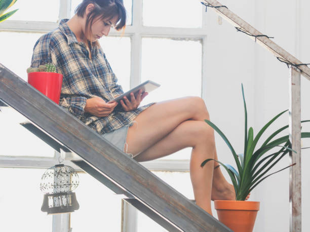 istock Woman on house stairs relaxing, reading email on a tablet 890850144