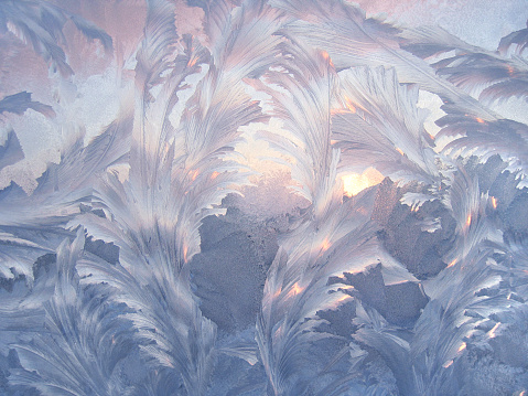 Beautiful ice pattern and sunlight close-up on winter window glass, natural background