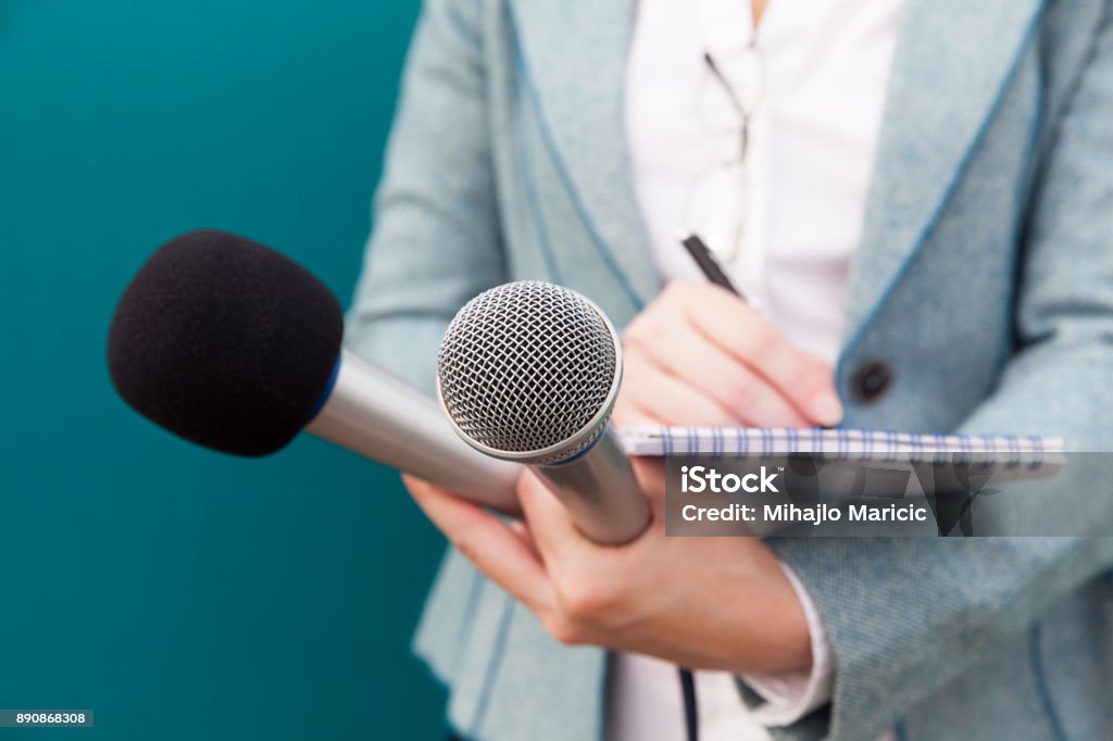 Female journalist at press conference, writing notes, holding microphone Female reporter taking notes at press conference Journalist Stock Photo