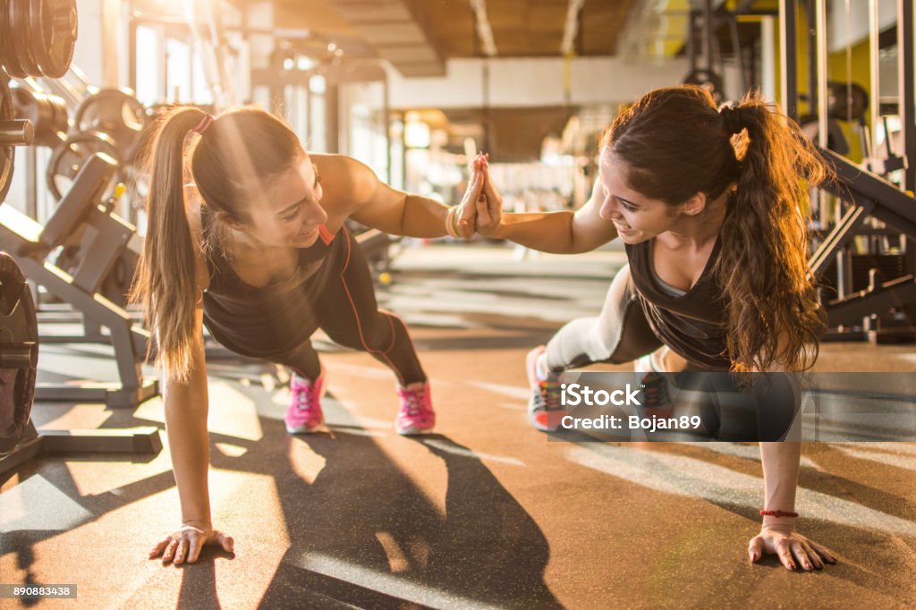 Sporty women giving high five to each other while working out together at gym. Gym Stock Photo